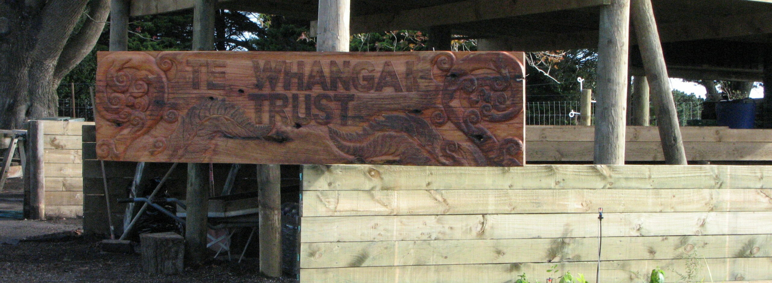 An image of Te Whangai Trust signage carved from a slab of macracarpa by trainees' Whanau.